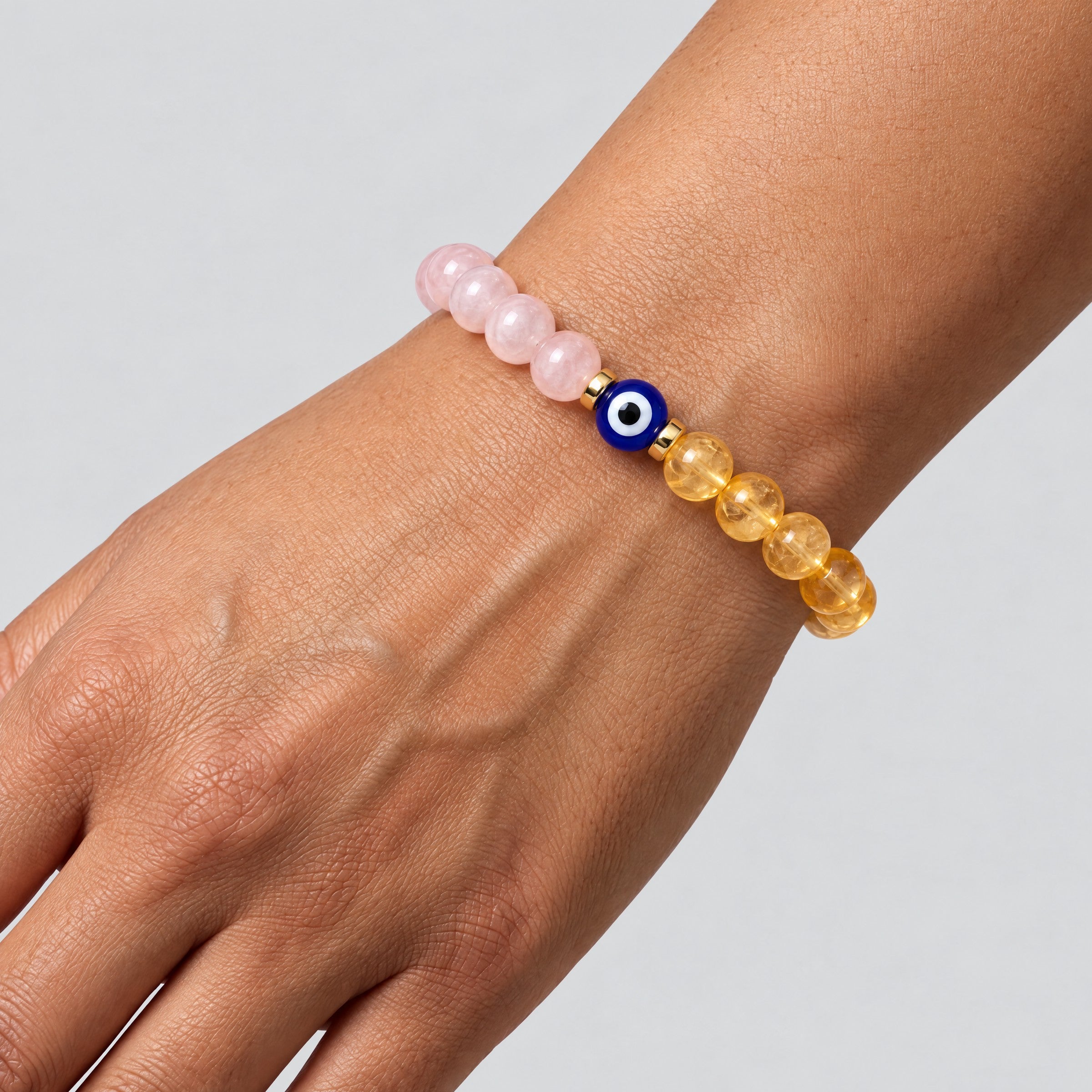 Rose quartz and citrine evil eye bracelet worn on a wrist with the blue eye bead centered between the two stone halves.