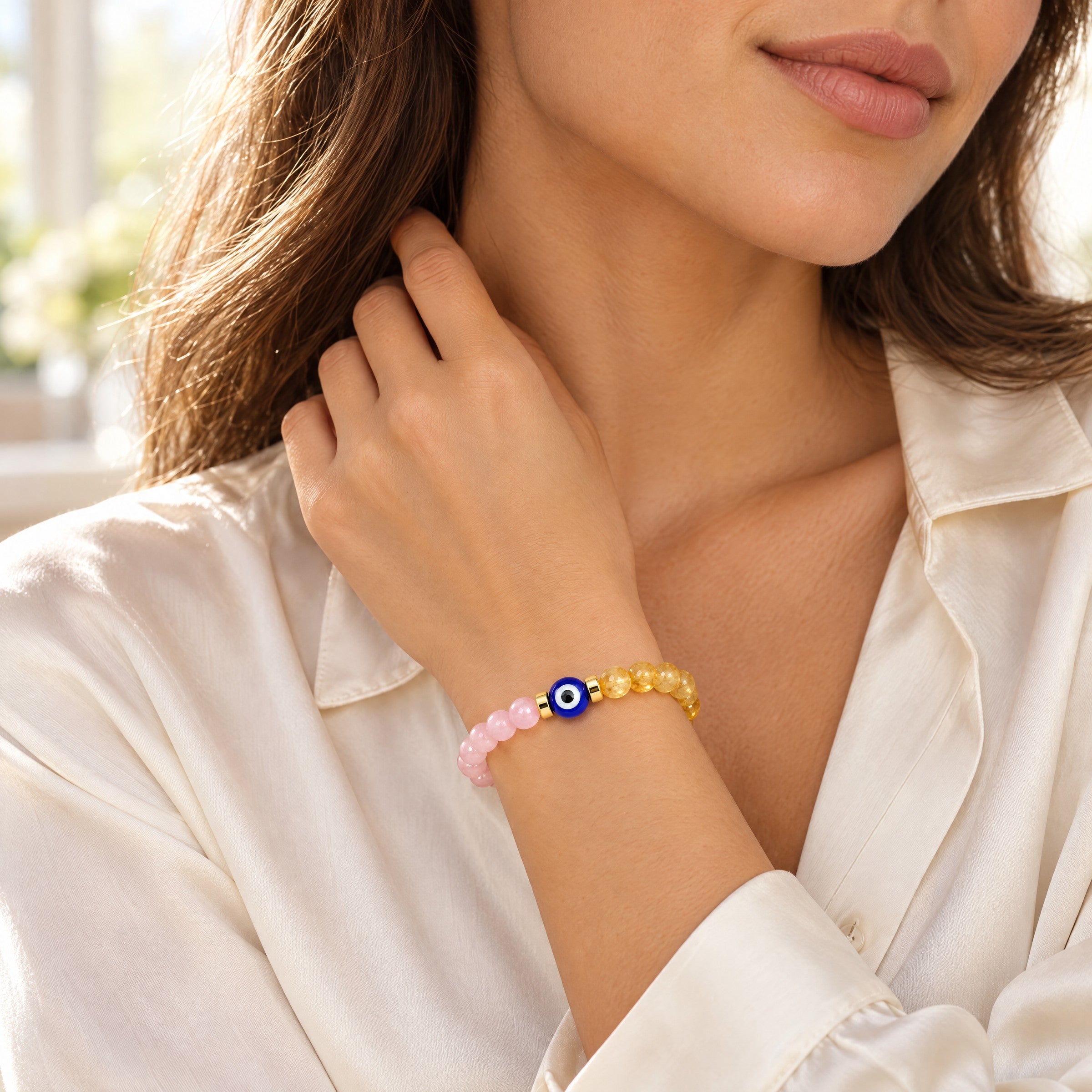 Woman wearing the rose quartz and citrine evil eye bracelet with a white blouse in a soft lifestyle setting.