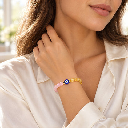 Woman wearing the rose quartz and citrine evil eye bracelet with a white blouse in a soft lifestyle setting.